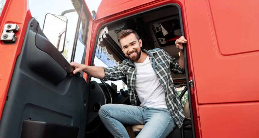Young smiling male truck driver inside his red cargo truck