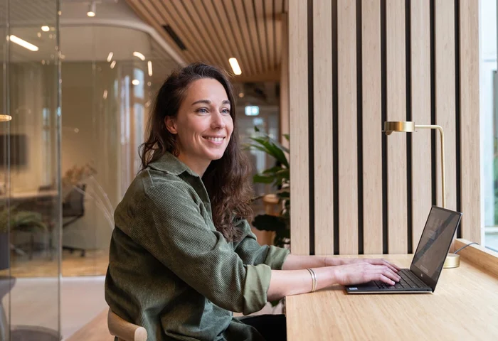 Employee sitting at a desk in front of a laptop looking out the window and smiling