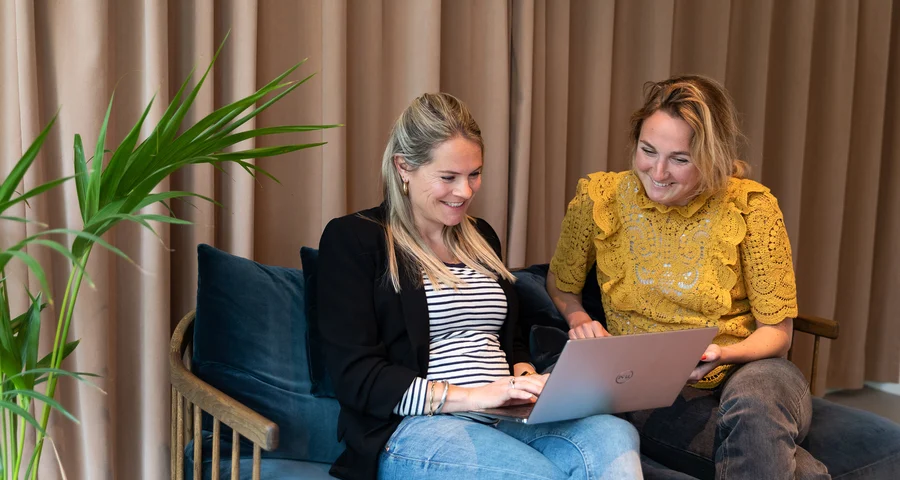 Två kvinnor som sitter i en soffa och kollar på en dator
