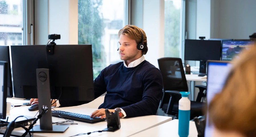 Kantoormedewerker met een headset die op een computer werkt